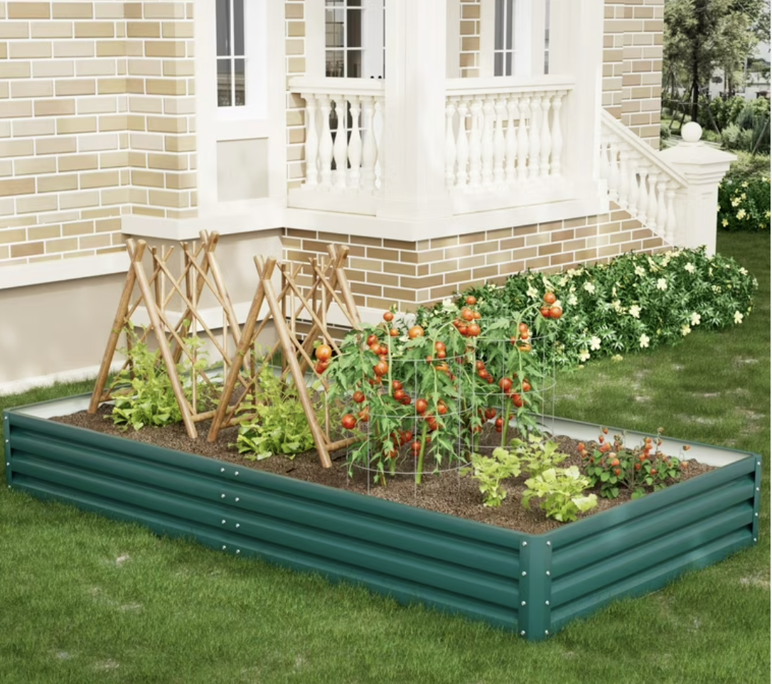 Modern green galvanized steel raised garden bed against a brick home, planted with tomatoes and lettuces.